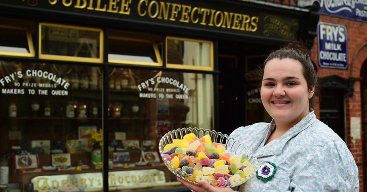 Beamish Museum staff member stands outside 1900s sweet shop holding traditional sweets.